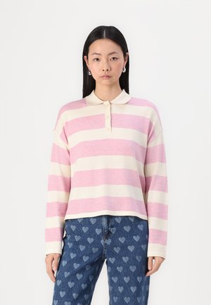 Striped long-sleeve polo in soft pink and cream fabric with a collar and four button placket. Paired with heart-patterned denim jeans.