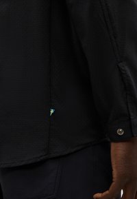 Κλείσιμο ενός χεριού δίπλα σε μαύρο υφασμάτινο πουκάμισο με μικρό ταμπελάκι της Σουηδικής σημαίας κοντά στο τελείωμα.