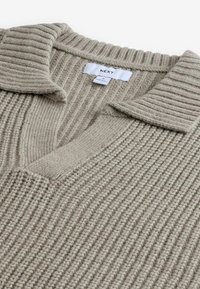 Beige strikket sweater med ribbet tekstur, der har en V-hals og flad krave. Stoffet ser blødt og varmt ud. Bredmærke synligt.