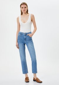 Vit ribbad bodysuit kombinerad med ljusblå högmidjade jeans. Modellen bär bruna loafers. Enkelt design, figursydd silhuett och en avslappnad look.