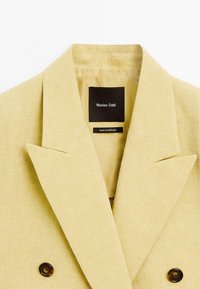 Helles gelbes Blazer mit Reverskragen, ausgestattet mit zwei schwarzen Knöpfen und einem Etikett, das "Massimo Dutti, Made in Portugal" liest.