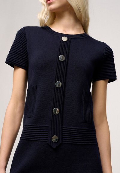 Cardigan a maglia di colore blu navy con maniche corte a coste, dotato di chiusura con bottoni argentati e due tasche texturizzate sul davanti.