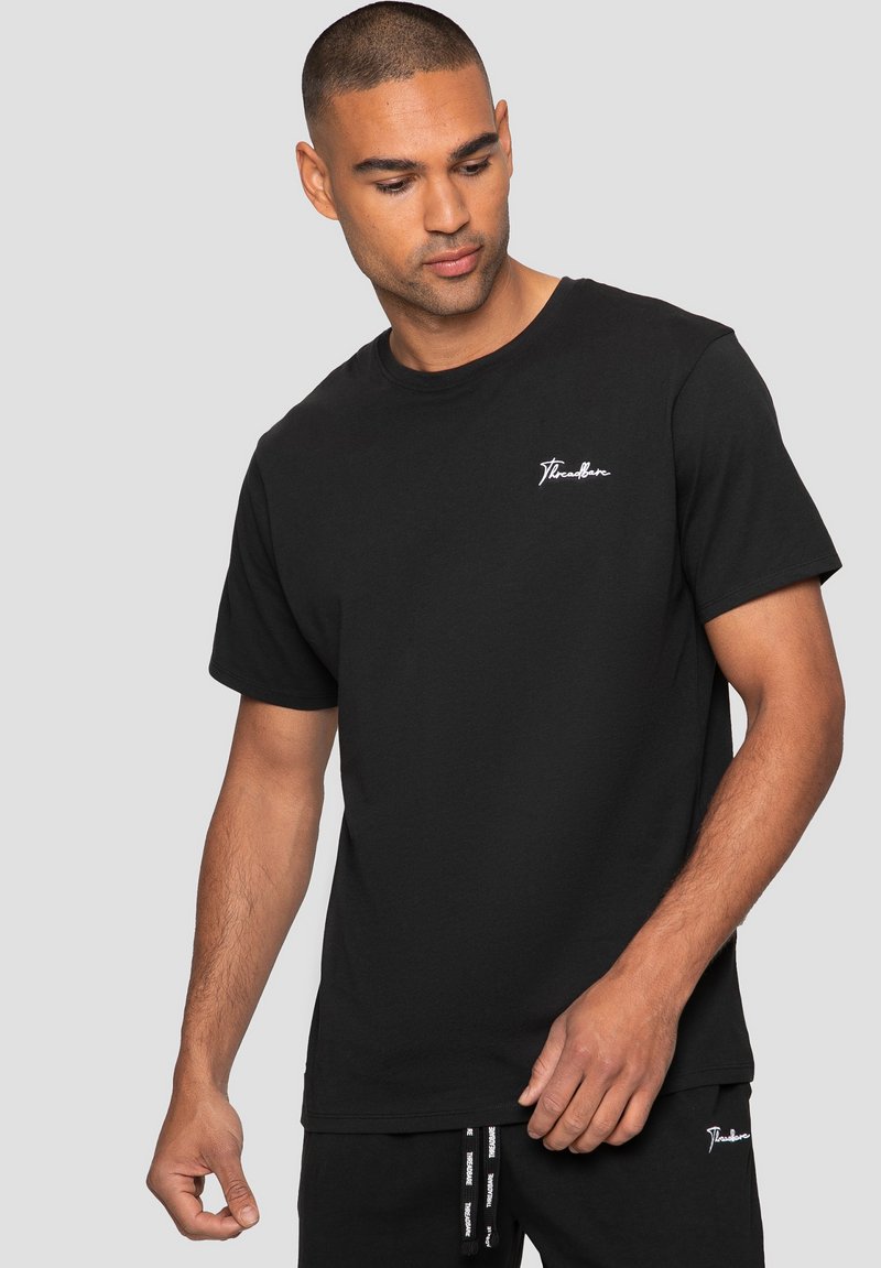 T-shirt en coton noir avec col rond, manches courtes et un petit logo brodé blanc sur la poitrine gauche. Texture lisse et coupe décontractée.