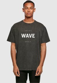 Zwarte oversized t-shirt met denimlook, met op de voorkant witte tekst "LIFE IS A WAVE CATCH IT", met korte mouwen en een ronde hals.