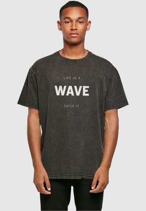 Black oversized t-shirt in denim look, featuring white text "LIFE IS A WAVE CATCH IT" on the front, with short sleeves and round neck.