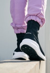 Schwarze Slip-On-Sneaker mit einem strukturierten Mesh-Obermaterial und einer weißen Gummisohle. Enthält ein Logo an der Seite und ein elegantes Design.