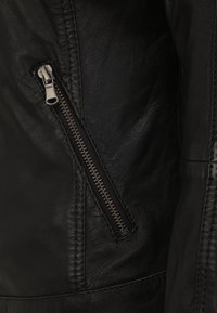 Schwarze Lederjacke mit einer Reißverschlusstasche und Metallbeschlägen, strukturiertem Obermaterial und sichtbaren Nähten entlang der Nähte.
