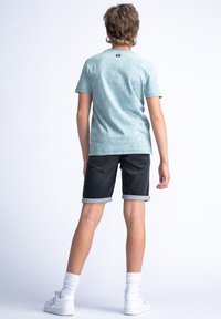 Camiseta de algodón azul claro con estampado, pantalones cortos de mezclilla negra con puños enrollados, calcetines blancos y zapatillas blancas. Vista trasera, diseño minimalista.