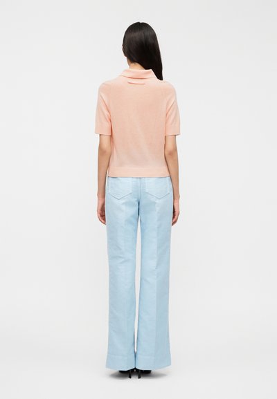 Ροζ ανοιχτό ροζ κοντομάνικο πόλο πουκάμισο από μαλακό ύφασμα, συνδυασμένο με ψηλόμεσα ανοιχτό μπλε παντελόνια με φαρδιά μπατζάκια, και ορατές πίσω τσέπες.