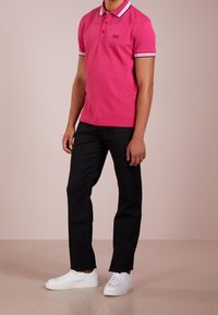 Rosa polo t-shirt med krage, kontrasterande randiga ärmar och en logotyp på bröstet, tillsammans med svarta byxor och vita sneakers.