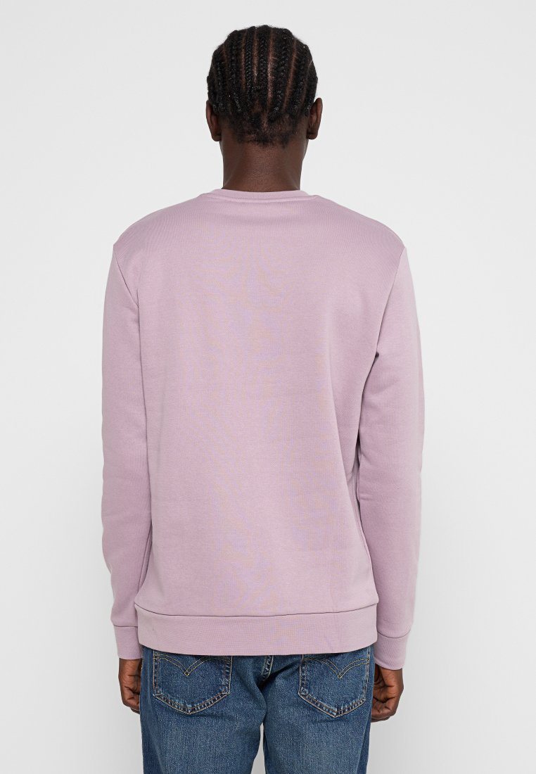 Felpa viola chiaro con collo e polsini a costine, realizzata in tessuto morbido. Presenta un orlo cucito e una vestibilità rilassata, abbinata a jeans blu.