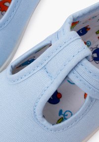 Scarpe di tela azzurre chiaro con design a tagli, cuciture a contrasto e interno a fantasia con colorati personaggi dei cartoni animati.