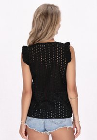 Top nero senza maniche con spalline arricciate e piccoli motivi ritagliati, realizzato in tessuto leggero, abbinato a pantaloni shorts in denim.