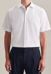 Bílá košile s krátkým rukávem, zapínaná na knoflíky, s límečkem a jednou náprsní kapsou, vyrobená z hladké látky s jemným leskem.
