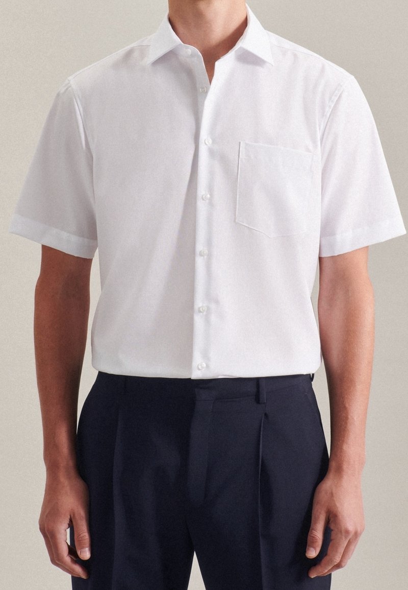Bílá košile s krátkým rukávem, zapínaná na knoflíky, s límečkem a jednou náprsní kapsou, vyrobená z hladké látky s jemným leskem.
