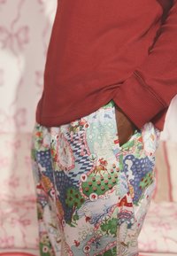 Czerwona bluzka z długim rękawem w połączeniu z kolorowymi, wzorzystymi spodniami do wypoczynku, ozdobionymi motywami świątecznymi, drzewkami i scenkami na jasno niebieskim tle.