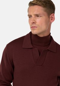Maglione a maglia color bordeaux con colletto a coste e design a V. Presenta una finitura testurizzata, una vestibilità leggermente ampia e maniche lunghe.