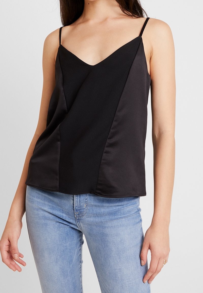 Débardeur noir avec un décolleté en V, de fines bretelles et une texture lisse avec des détails de panneaux. Associé à un jean bleu clair.