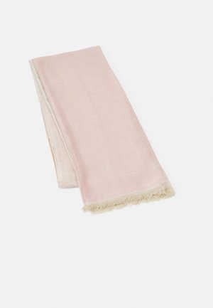 Serviette rose pâle douce pliée avec des bords à franges beige posée sur un fond blanc uni.