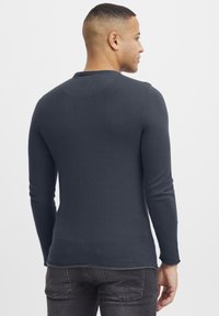 Maglietta a maniche lunghe grigio scuro con un design aderente e texture a coste, caratterizzata da un collo rotondo e dettagli di cucitura sottili sulle cuciture.