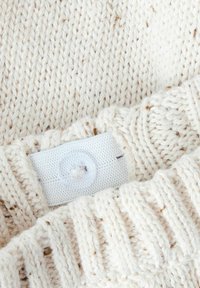 Pull en tricot crème avec des points texturés et un ourlet côtelé ; présente une étiquette blanche avec un détail de bouton.
