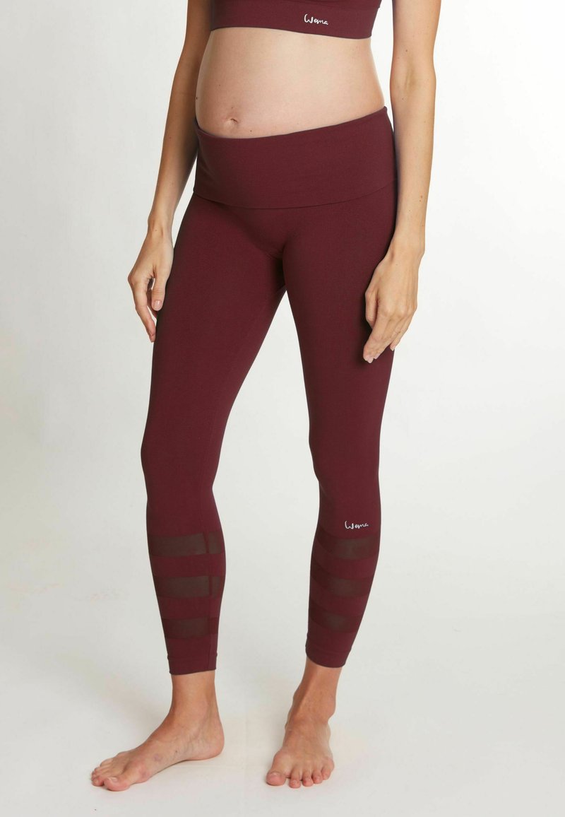 Leggings de maternité en tissu bordeaux extensible, avec une large ceinture et des accents de bandes en maille transparente le long des jambes inférieures.