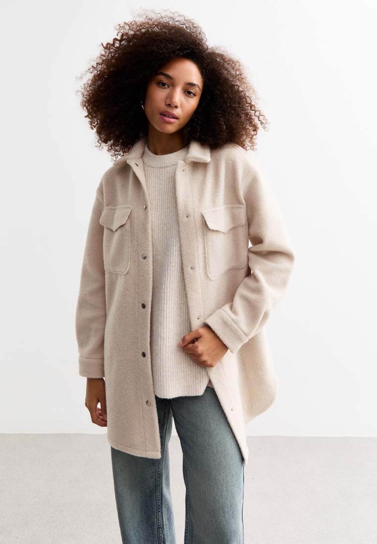 Chaqueta de camisa de mezcla de lana color beige con dos bolsillos en el pecho, cierre de botones y corte relajado, superpuesta sobre un suéter texturizado claro y jeans de mezclilla.