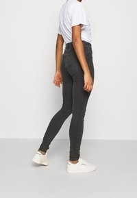 Jeans negros de talle alto hechos de denim, con un diseño ajustado, estilo de cinco bolsillos y detalles de costura sutiles. Combinados con zapatillas blancas.