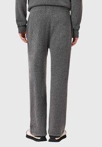 Szare spodnie z mieszanki wełny o luźnym kroju, z płaskim paskiem i subtelną fakturą. Widoczne przeszycia na mankietach i kieszeniach.