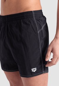 Pantaloni da bagno neri realizzati in tessuto leggero, dotati di vita elastica e cuciture bianche a contrasto. Include il dettaglio del logo 'arena'.
