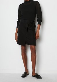 Sort strikket trøje med høj hals og lange ærmer; kombineret med en sort omslagsnederdel med sløjfedetalje og glat tekstur.