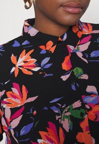 Chemise florale avec un fond noir, ornée de fleurs vibrantes orange, roses et bleues. Col classique, fermeture à boutons, texture de tissu lisse.