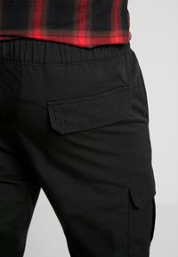 Schwarze Cargo-Hosen mit einer Gesäßtasche mit Klappe, aus leichtem Stoff und einem elastischen Bund für zusätzlichen Komfort.
