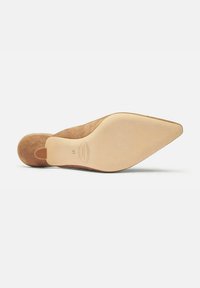 Zapato de punto con puntera afilada en gamuza color topo. Presenta una suela ligera de color suave con un pequeño tacón y una marca de tamaño en relieve.