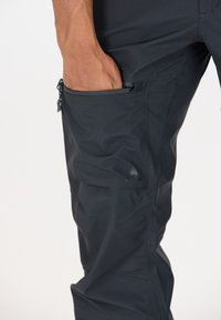 Pantalons de plein air noirs avec une texture lisse, comportant une poche latérale zippée et un logo sur la jambe inférieure. Design ajusté, matériau léger.