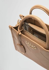 Bolso de mano de imitación cuero beige con herrajes dorados, exterior texturizado, asas dobles y compartimentos con cremallera en el interior. Presenta un detalle de logo.