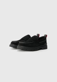 Crne slip-on cipele s nubuk gornjištem, podstavljenim gležnjem, elastičnim trakama i teksturiranom gumiranom potplatom s rebrima. Crveni detalji na peti.