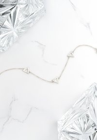 Silver kedja med geometriska triangelberlockar med utskurna mitt, mot en marmorerad vit bakgrund.