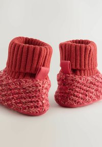 Punaiset neuleiset tossut, joissa on ribattu varsi. Tossuissa on teksturoitu kudontakuvio ja pieniä kangassilmukoita helpompaa pukemista varten. Pehmeää ja mukavaa materiaalia.