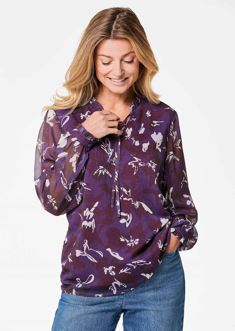 Blusa viola con stampa floreale, in tessuto leggero, maniche lunghe e mezza abbottonatura. Sfumature di polsini elastici e vestibilità comoda.
