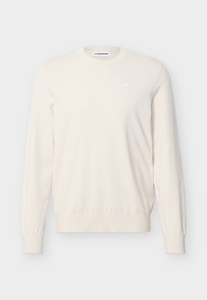 Kermanvärinen, pitkähihainen pyöreäkauluksinen neulepaita, jossa on resorit hihansuissa ja helmassa. Vasemmassa rinnassa pieni valkoinen logo ja kauluksen sisäpuolella bränditunniste.