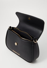 Borsa a tracolla in pelle nera con design a pattina, accessori in oro e logo. All'interno presenta due scomparti con cerniera. Texture liscia.