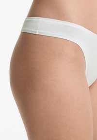 Witte katoenen stringonderbroek met een soepele textuur en brede elastische tailleband, met een close-up van het heup- en dijgebied.
