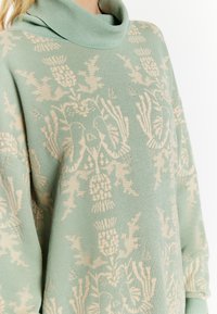Mint green sweater with a cowl neck, featuring a beige floral and animal pattern. Made of soft knit fabric, loose fit for comfort.