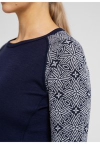 Marineblå langærmet top med et struktureret, mønstret grå ærme med geometriske designs. Glat stof og kontrasterende farveaccenter.