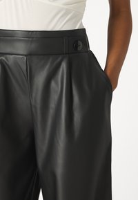 Black leather trousers with a smooth texture, pleated front design, wide legs, and a black button accent at the waistband and side pockets.