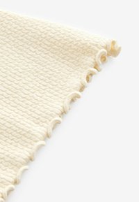 Tessuto di cotone texturizzato color crema con un motivo ondulato e bordi scallop, mostrato in un angolo per evidenziare i dettagli.
