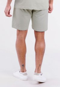 Lichtgroene shorts van zacht materiaal, met een eenvoudig ontwerp, gedragen met witte sneakers. Zichtbare been tattoos en vlakke naden.