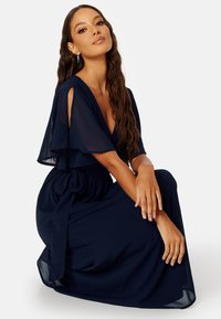 Tmavě modrá maxi šaty vyrobené z lehkého materiálu, s hlubokým výstřihem do V, volnými rukávy a vázaným pasem pro elegantní siluetu.