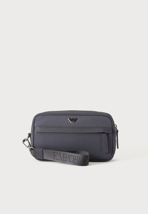Petite pochette gris foncé compacte avec poche avant zippée, logo en métal, et sangle tissée imprimée avec "EMPORIO."